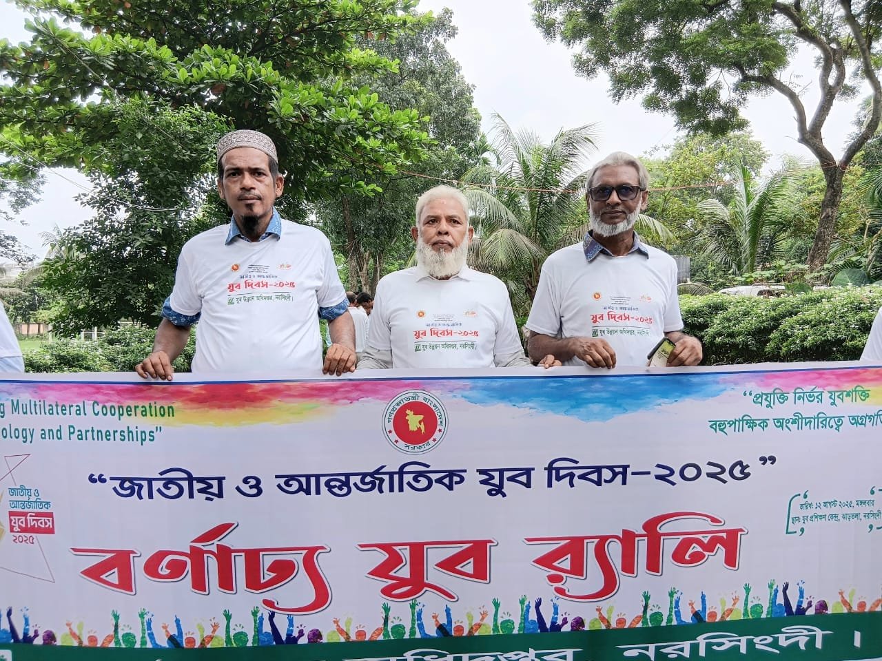 Youth rally; three leaders in white shirts in front of banner.